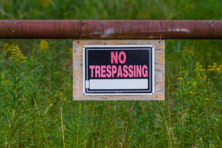 no trespassing sign hanging on an iron pipe